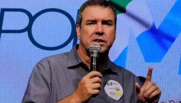 Homem falando ao microfone com o dedo indicador levantado.