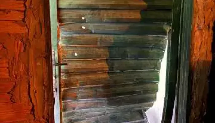 Porta de metal danificada e amassada em parede de tijolos.