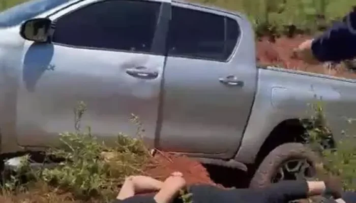 Homem detido no chão próximo a uma caminhonete prata.