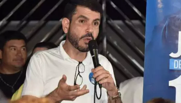 Homem de camisa branca discursando com microfone em evento.