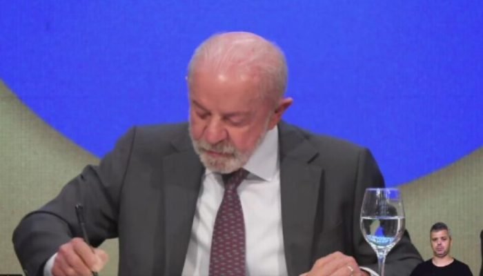 Presidente Lula assinando um documento oficial em uma mesa.