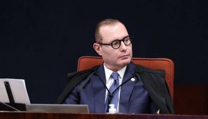 Homem de óculos e toga preta sentado em tribunal.