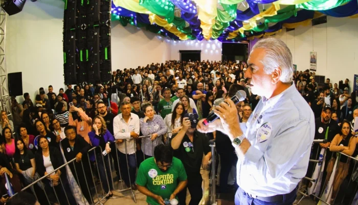 Homem discursando para grande multidão em evento com cores do Brasil.