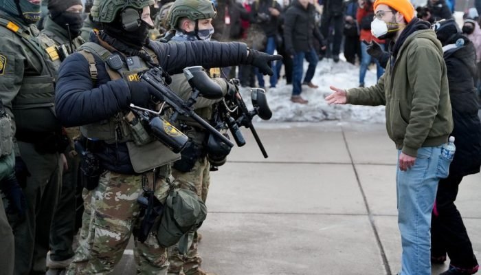 Agente federal e manifestante gesticulam durante protesto contra o assassinato —