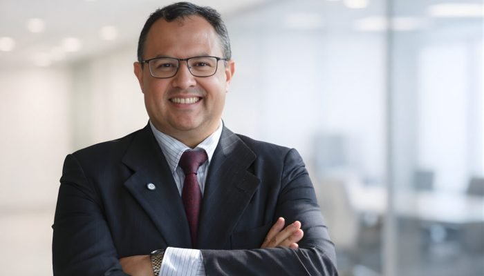 Executivo sorridente de óculos e terno em ambiente corporativo.