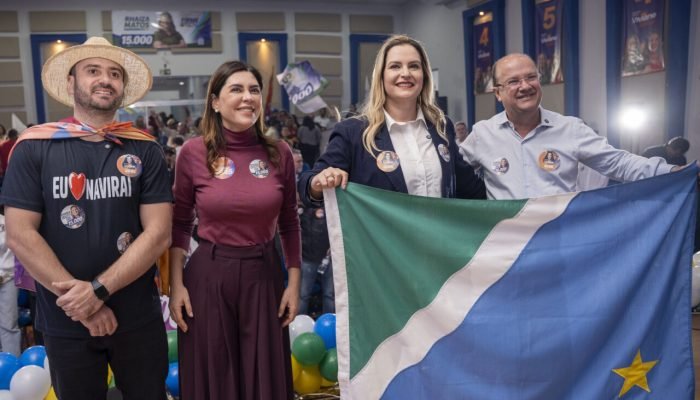 Quatro pessoas sorridentes segurando a bandeira de Mato Grosso do Sul.
