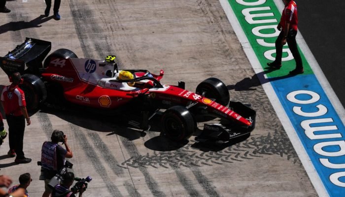 Carro Ferrari F1 número 44 no pit lane com fotógrafos.