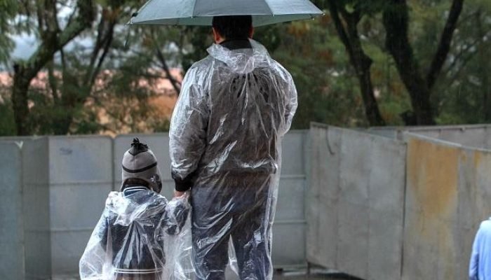 Homem segura mão de criança em dia chuva — Foto: Homem segura mão de criança em
