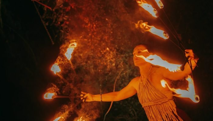 Mulher realizando performance artística com leques de fogo à noite.