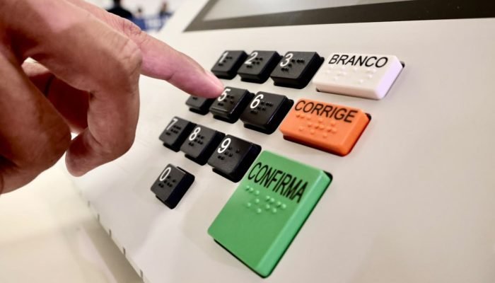 Mão pressionando tecla numérica em uma urna eletrônica brasileira.