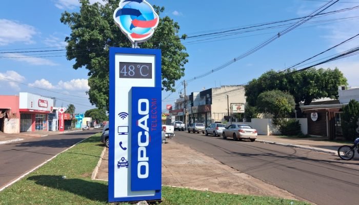 Totem da Opção Telecom marcando 48 graus em rua ensolarada.