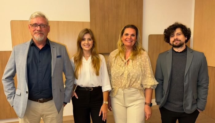 Quatro profissionais sorrindo em pé em um escritório moderno.