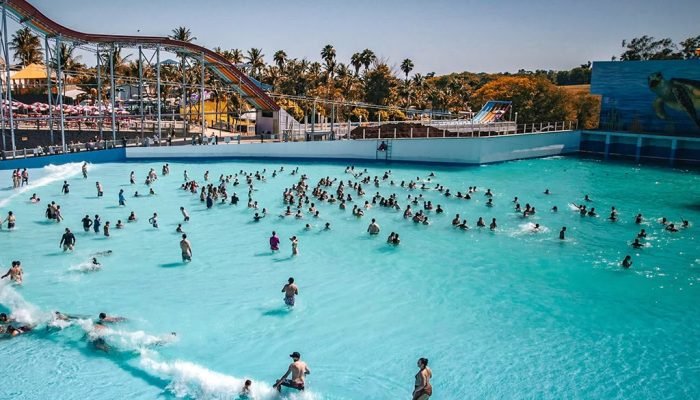 Piscina de ondas lotada em um parque aquático ensolarado.