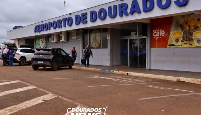 Fachada do Aeroporto de Dourados com carros e pessoas.