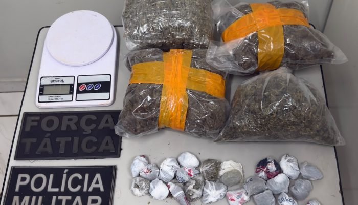 Drogas apreendidas, balança e insígnias da Polícia Militar sobre mesa.