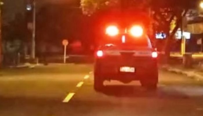 Viatura policial com luzes vermelhas acesas em rua escura.