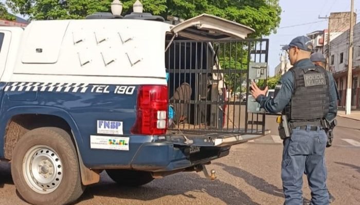 Policial militar fardado ao lado de viatura com compartimento aberto.