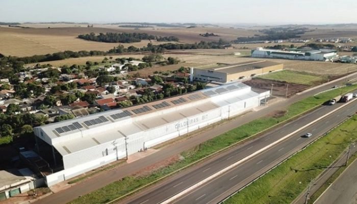 Vista aérea de galpão industrial com painéis solares na cobertura.
