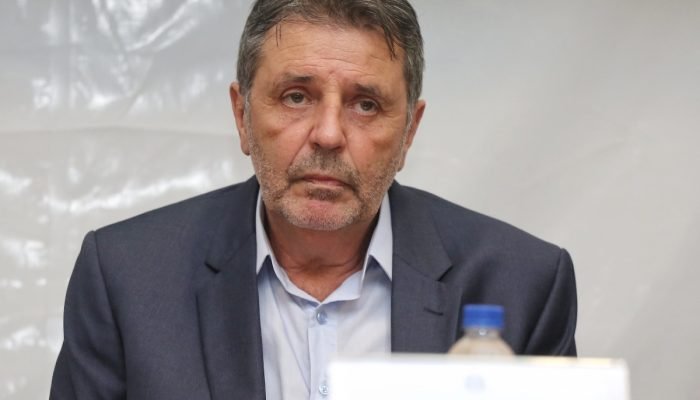 Homem de terno e camisa azul com expressão séria.