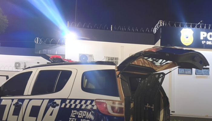 Viatura da polícia com porta-malas aberto em frente à delegacia.