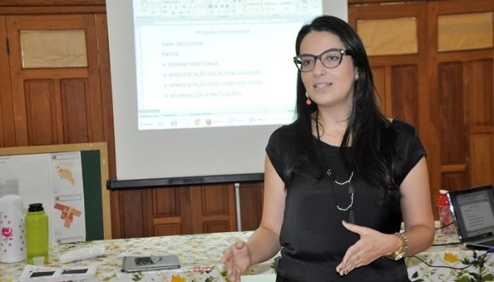 Mulher palestrando com tela de projeção ao fundo.