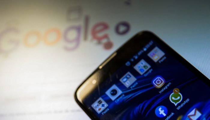 Smartphone com ícones de aplicativos e logotipo do Google ao fundo.