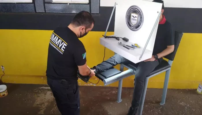 Servidor colocando tornozeleira eletrônica em homem (Foto: divulgação / Agepen)