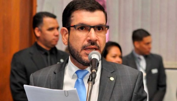 Homem de terno e óculos falando em um microfone.