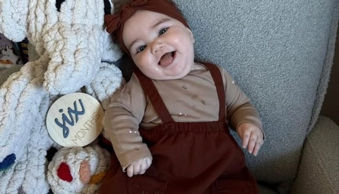 1 de 1 foto colorida de uma bebê sentada em uma poltrona sorrindo para a foto. —