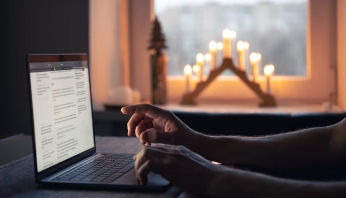 Pessoa usando laptop com decoração natalina iluminada ao fundo.