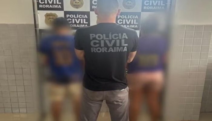 Policial civil de Roraima de costas entre duas pessoas desfocadas.