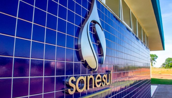 Logotipo metálico da Sanesul em uma parede de azulejos azuis.
