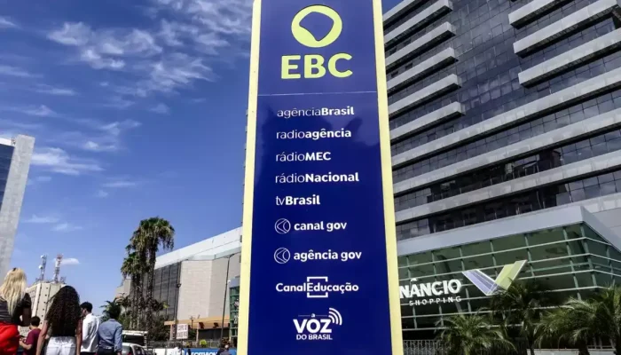 Totem azul da EBC em frente a um edifício moderno.