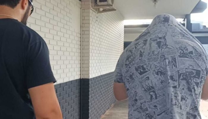 Suspeito é conduzido à delegacia após prisão — Foto: Suspeito, à direita, chegan