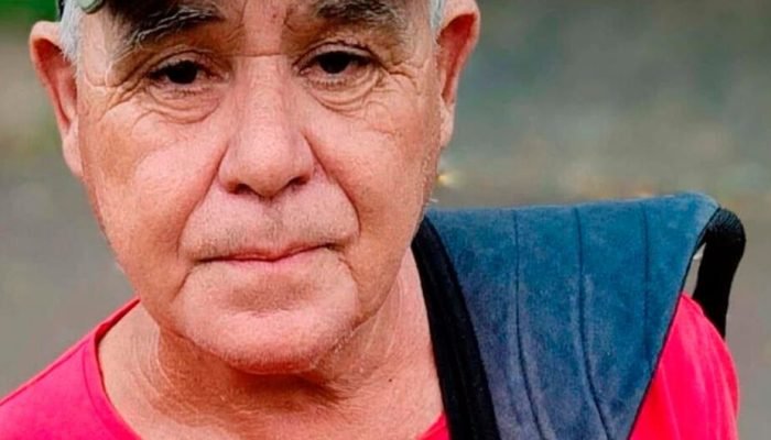 Homem idoso com expressão séria vestindo camiseta vermelha.